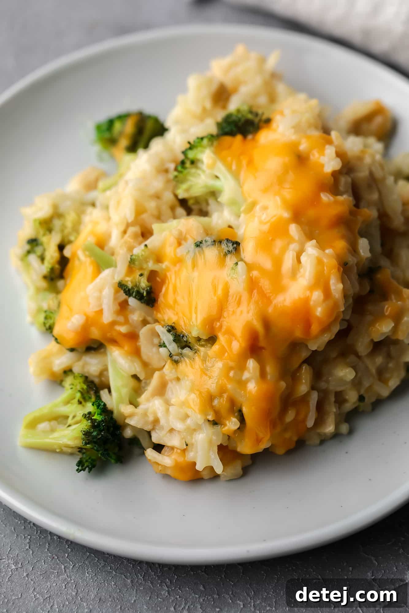 A scoop of creamy, cheese-covered vegan broccoli and rice casserole served on a small gray plate, ready to eat.
