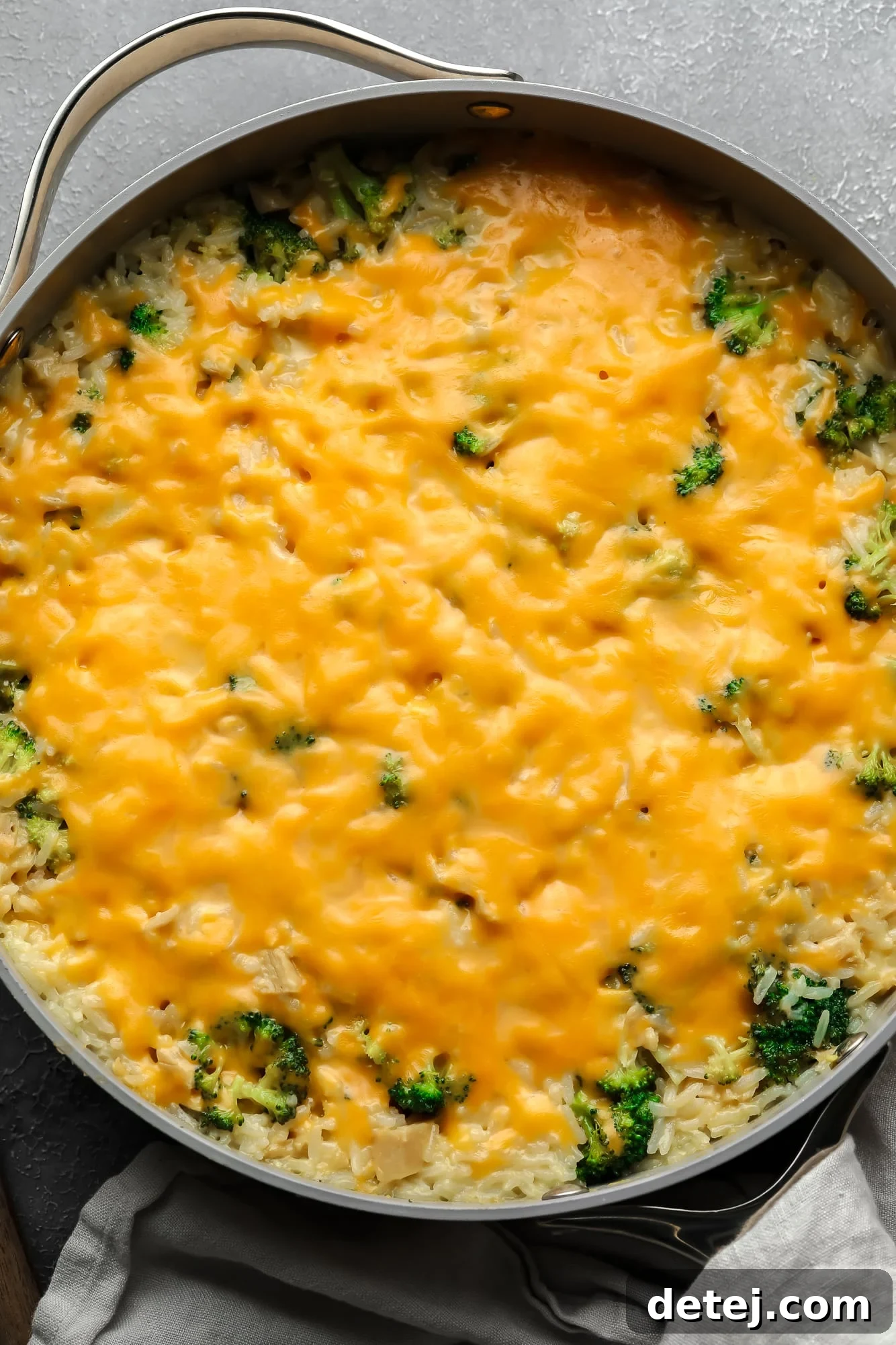 A large skillet filled with a bubbling, cheese-covered vegan broccoli and rice casserole, ready to be served.