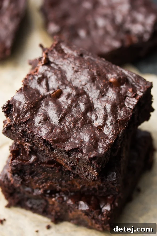 A perfectly stacked trio of fudgy vegan coconut oil brownies, showcasing their irresistible crinkle tops and rich, dark chocolate color. These dairy-free treats are a testament to easy, one-bowl baking.