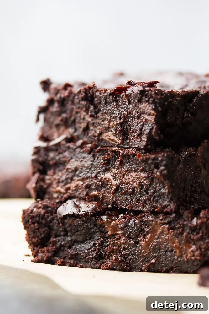 An enticing side-profile shot of three fudgy vegan coconut oil brownies, revealing their dense, moist interior texture and tall structure. Perfect for showcasing the delicious results of this easy, dairy-free recipe.