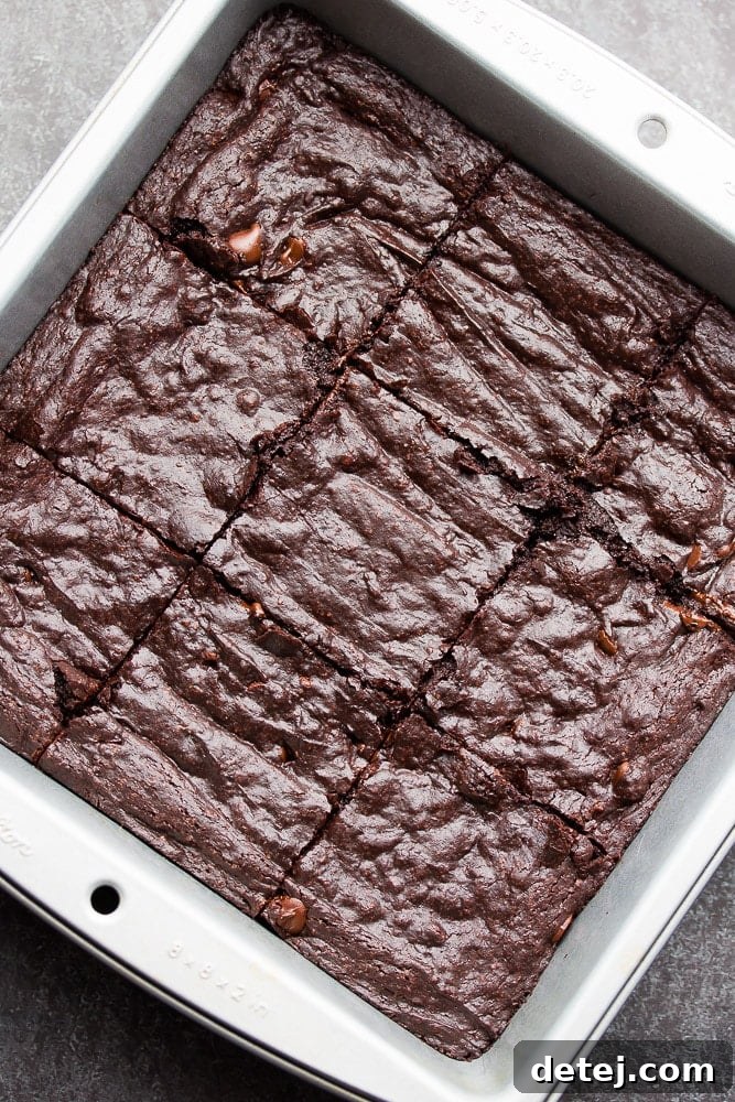 A top-down view of a baking pan filled with freshly baked, crinkly-topped vegan coconut oil brownies, perfectly cut into squares and ready to be enjoyed. Capturing the deliciousness of this one-bowl, dairy-free dessert.