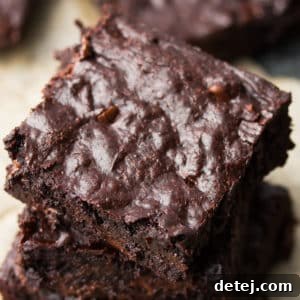 A close-up square image of a stack of fudgy vegan coconut oil brownies, showcasing their irresistible texture and perfect crinkle tops.
