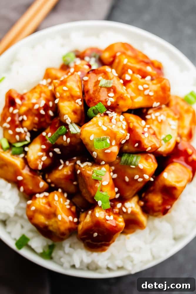 General Tso's Tofu served over white rice, garnished with sesame seeds and green onions.