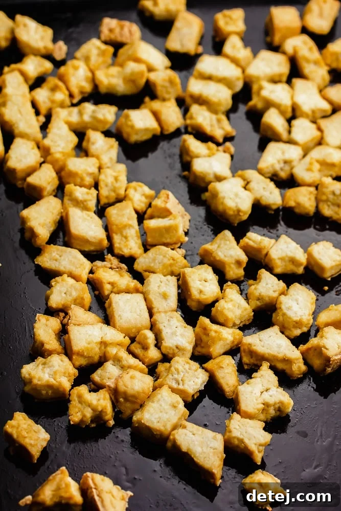 Crispy baked tofu pieces on a baking pan, ready to be sauced.