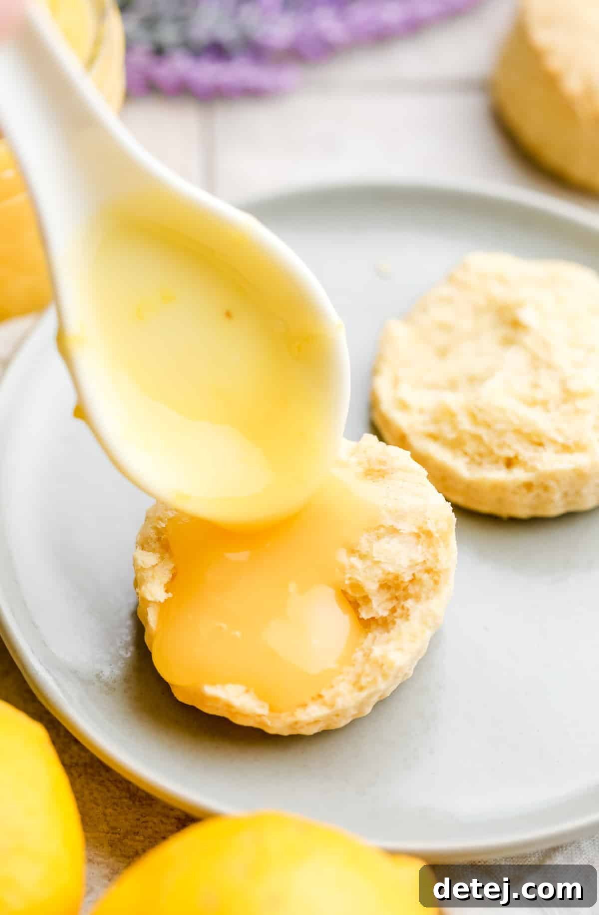 vegan lemon curd being spooned onto a plain round scone, lavender in background