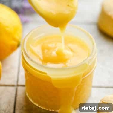 close up of lemon curd being drizzled into the jar with a white spoon on grey background