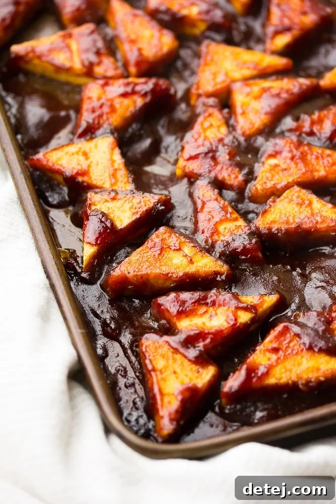 Close-up side view of perfectly cooked triangle BBQ tofu pieces, glazed with sauce, resting on a baking sheet, showcasing their crispy texture.