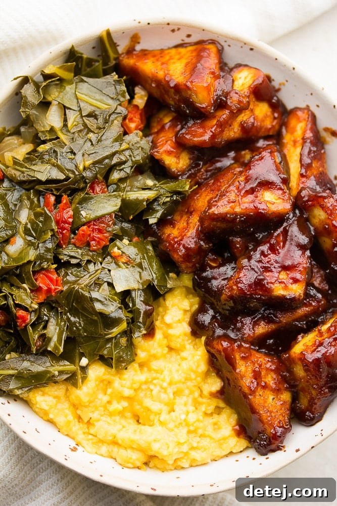 Very close-up view of a Southern Soul Bowl, showing the textures of crispy BBQ tofu, creamy grits, and vibrant collard greens.