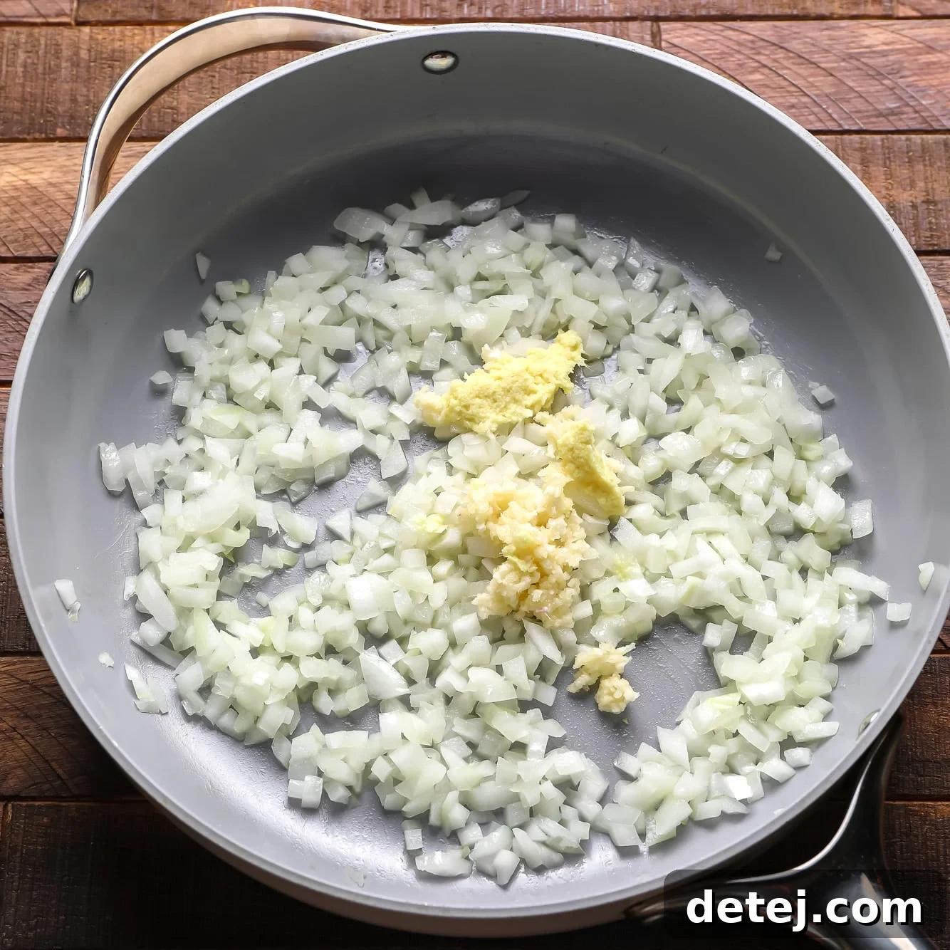 Chopped onions, garlic, and ginger cooking in olive oil in a large grey pan.