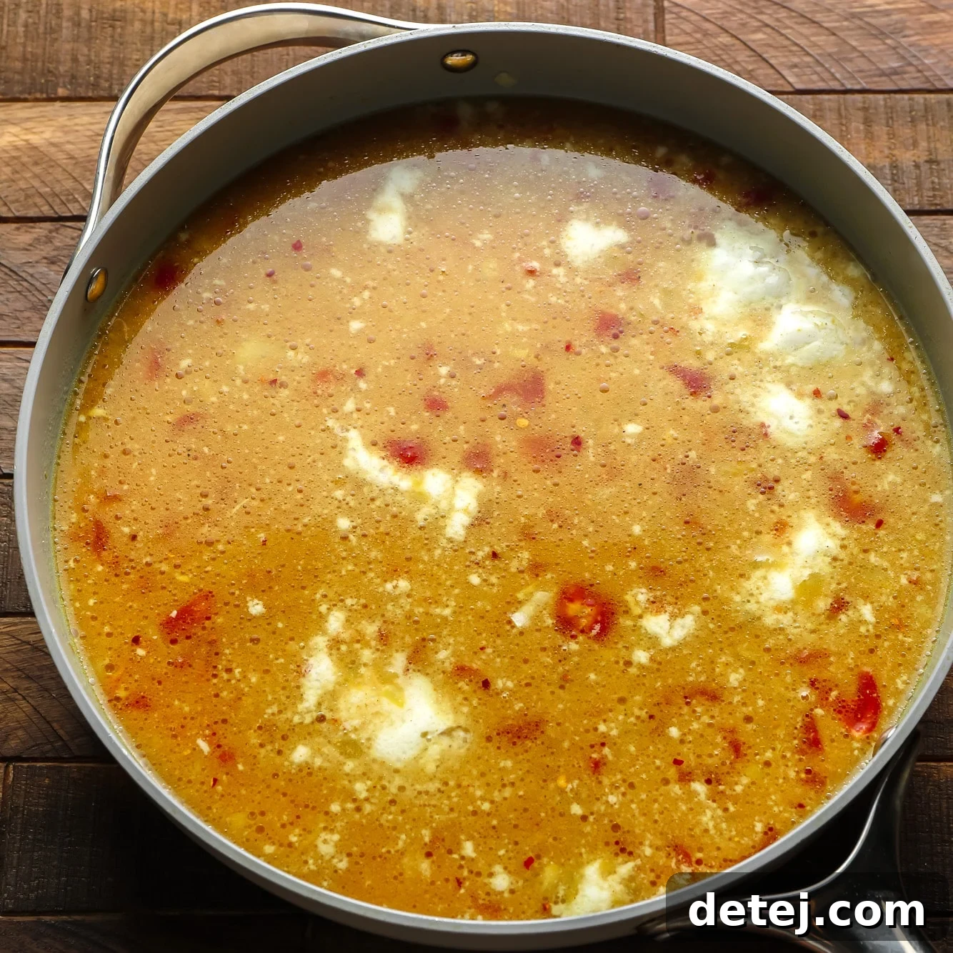 Uncooked red lentils, diced tomatoes, coconut milk, and vegetable broth combined in a large grey pot, before simmering.