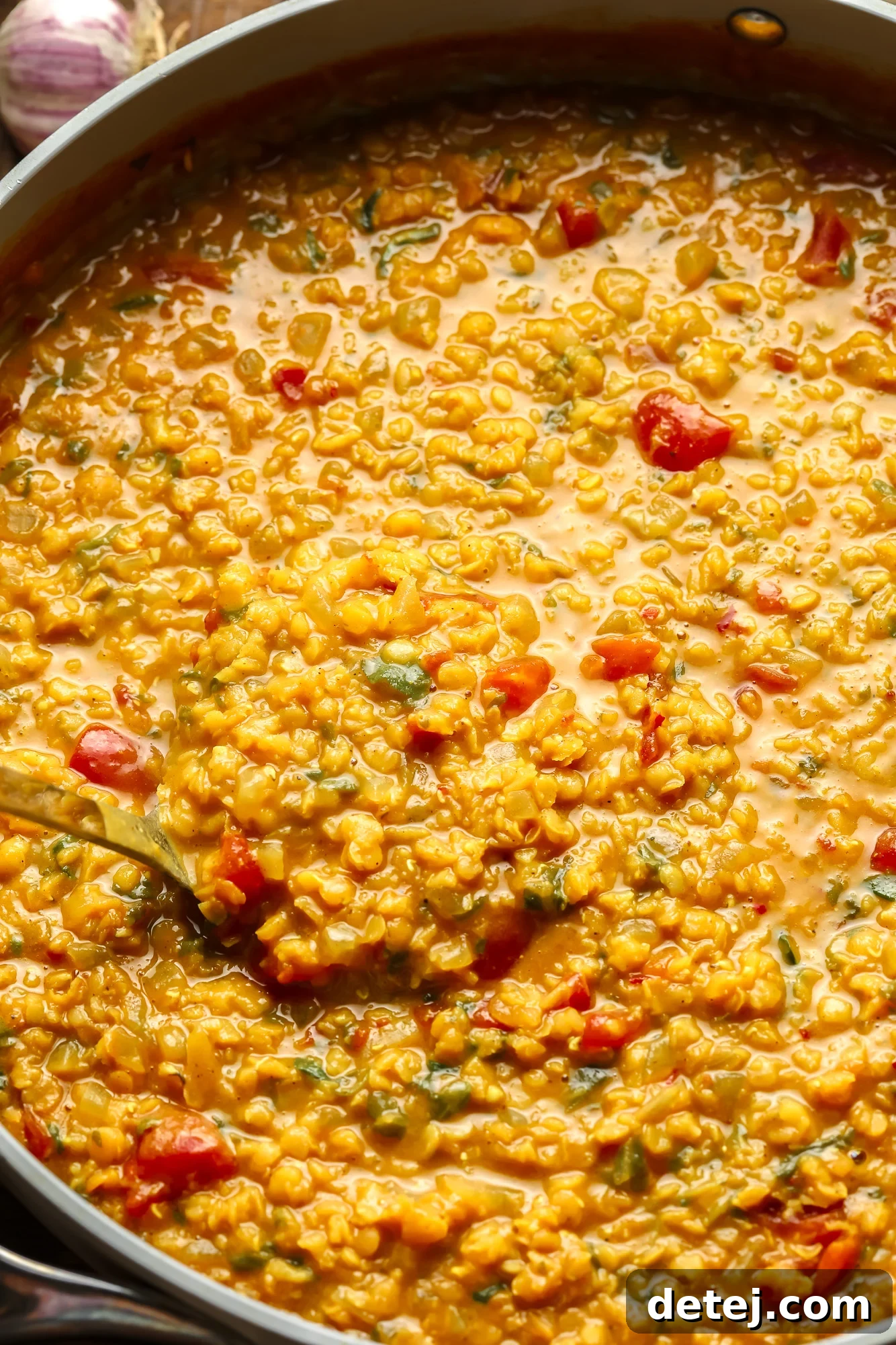 A spoon lifting a hearty scoop of red lentil dahl from a large pot, showcasing its creamy texture.