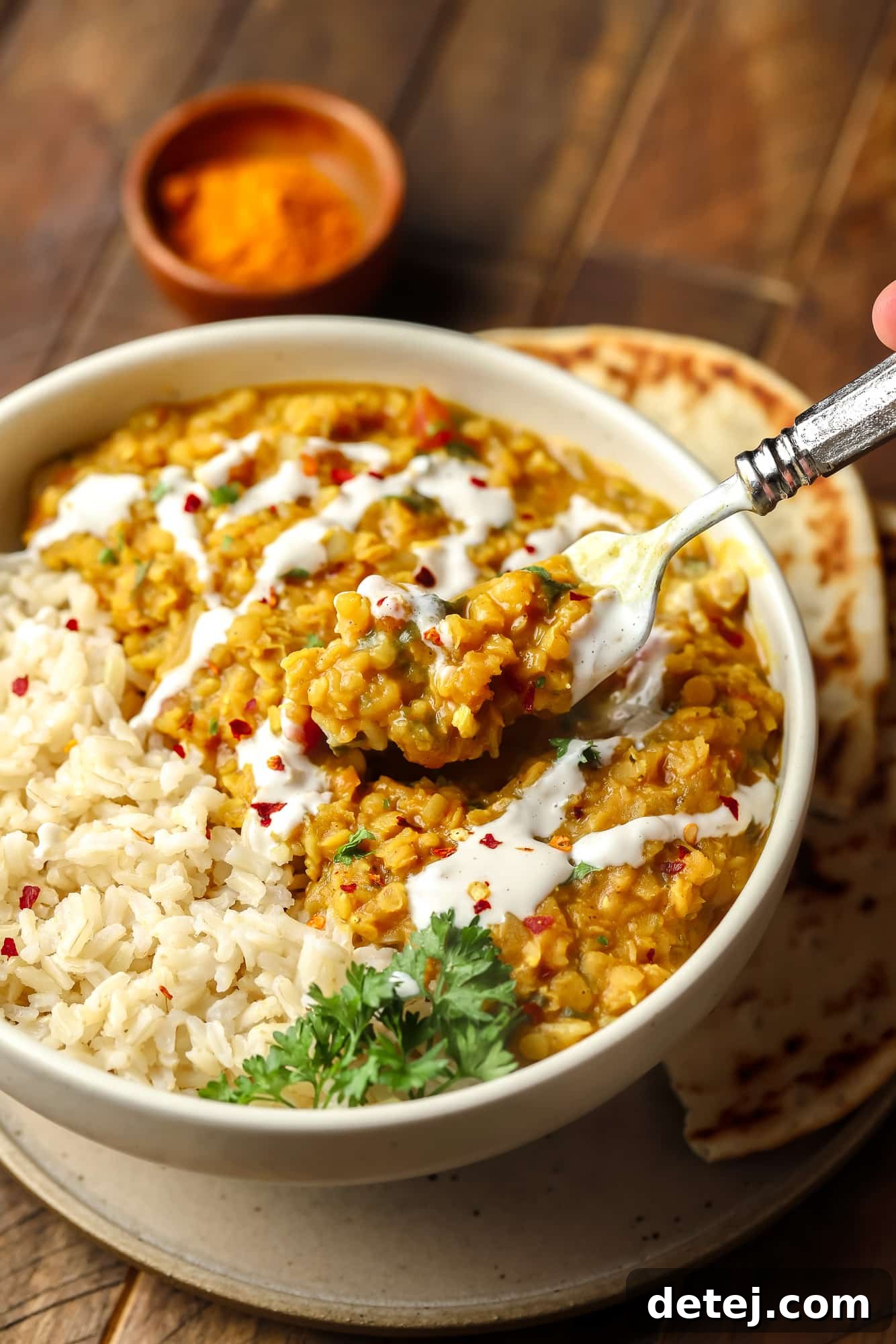 A fork lifting a scoop of red lentil dahl from a white bowl, showing its thick and creamy texture.