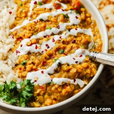 Close up on red lentil dahl topped with a drizzle of coconut milk and red chili flakes in a white bowl.