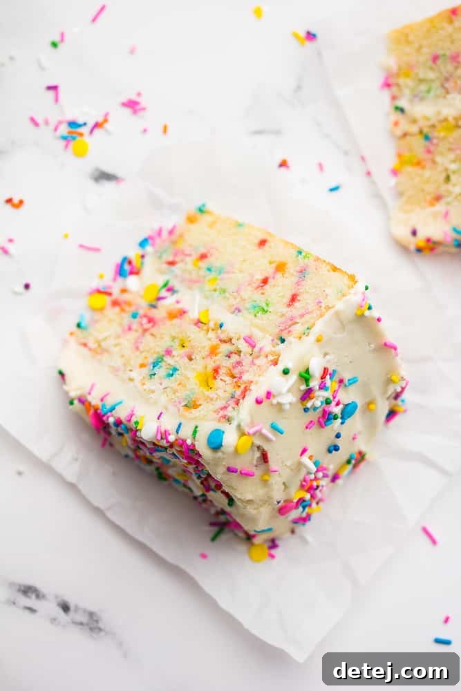 An overhead shot of a slice of vegan funfetti cake on a white plate, showcasing the colorful sprinkles embedded in the cake and frosting, ready to be enjoyed.
