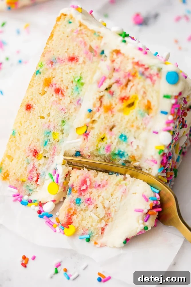A fork piercing a slice of Vegan Funfetti Cake, showcasing its moist interior, fluffy texture, and abundant colorful sprinkles. The cake is ready to be enjoyed.