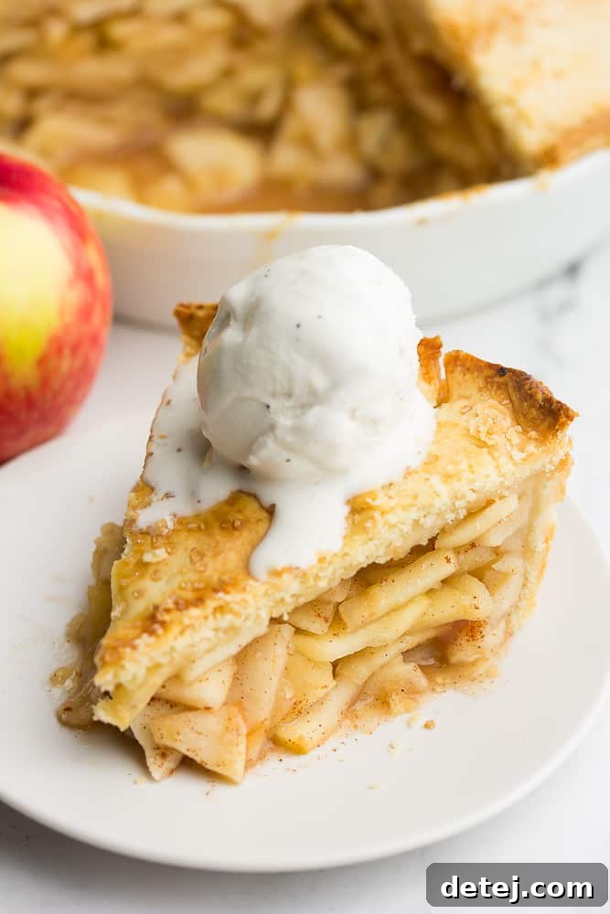 A delectable slice of vegan apple pie, served on a white plate with a scoop of melting vanilla non-dairy ice cream, ready to be enjoyed.