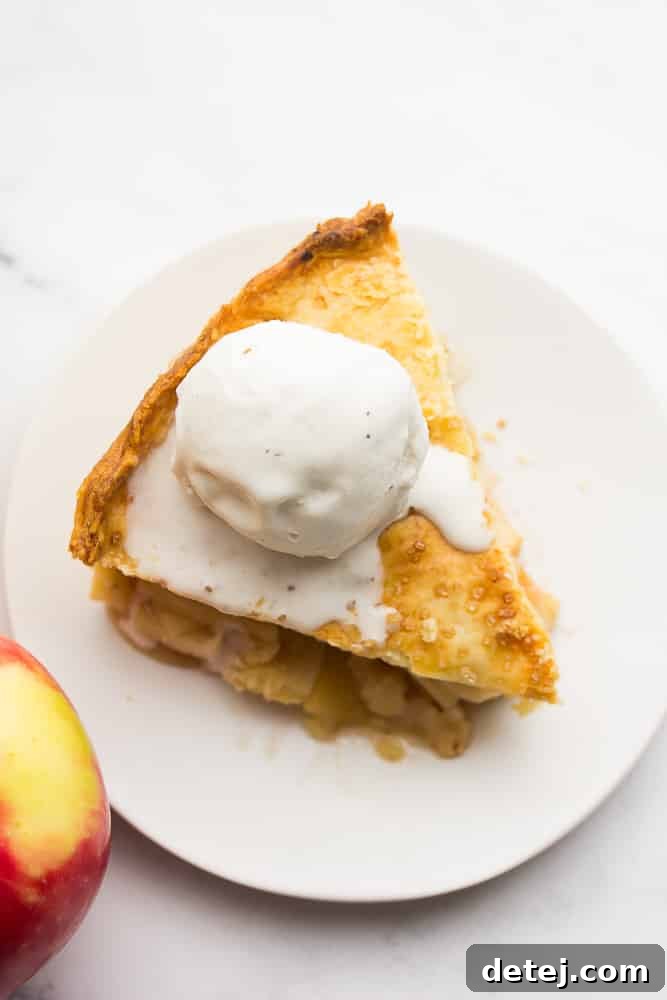 A close-up view looking down on a single slice of vegan apple pie on a plate, topped with a dollop of non-dairy vanilla ice cream.