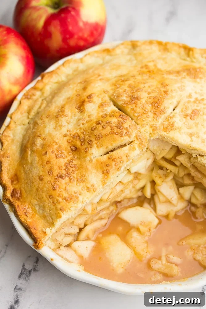 A perfectly baked vegan apple pie in a ceramic pie dish, with several slices already removed, revealing the generous, spiced apple filling within.
