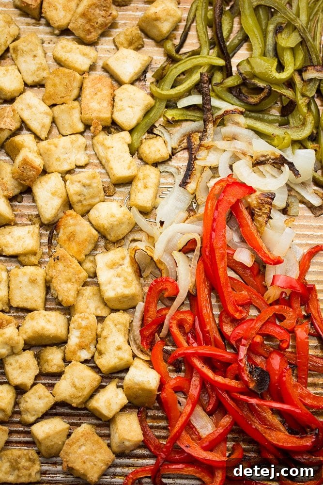 A sheet pan loaded with perfectly baked, golden-brown tofu chik'n pieces, brightly colored red and green bell peppers, and tender sliced onions.
