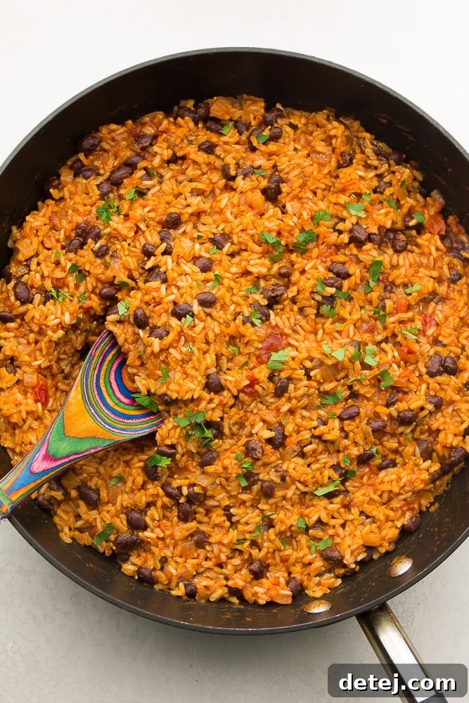 dark pan filled with rice and beans, cilantro on top, colorful spoon in it