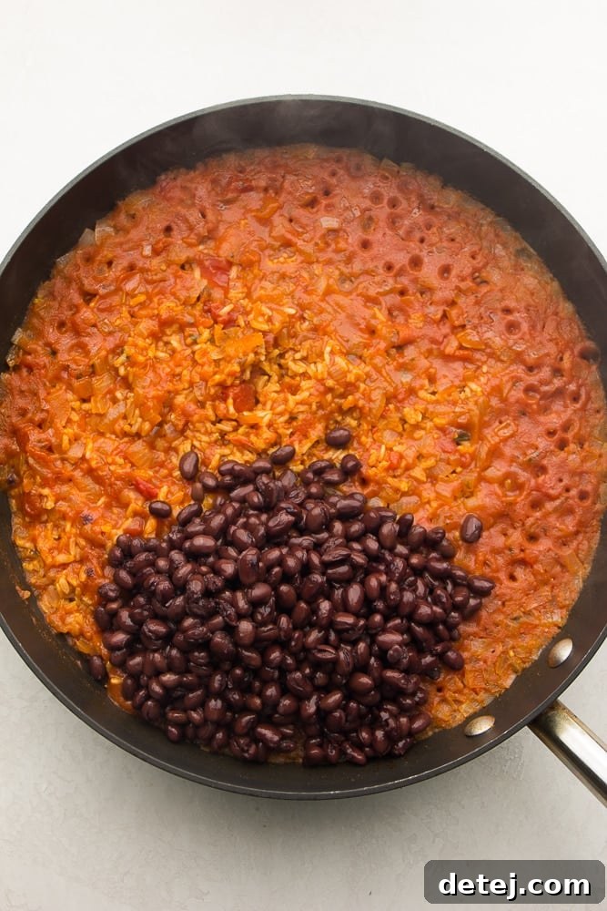 cooked red rice in a pan, adding black beans to it