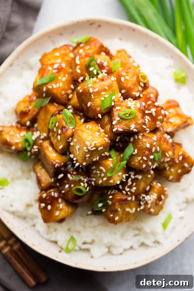 close up of a bowl of crispy sesame tofu served over rice, garnished with green onions and sesame seeds