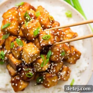 square image of a bowl of rice and saucy tofu, sesame seeds and green onions on top
