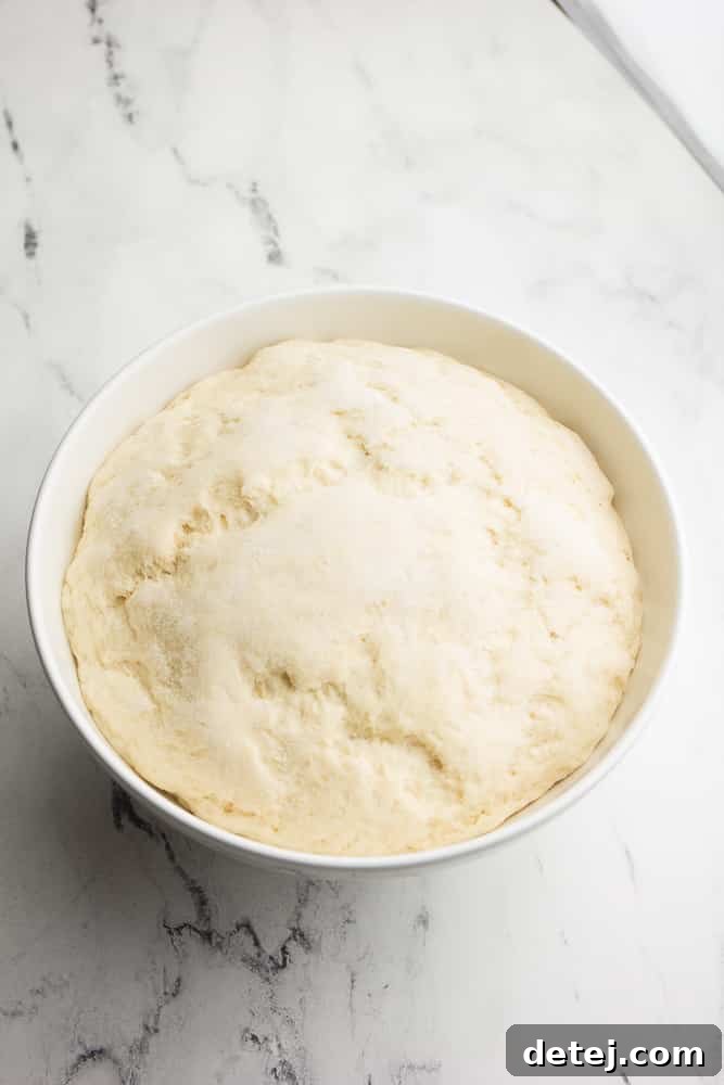 Risen pizza dough in a large white bowl