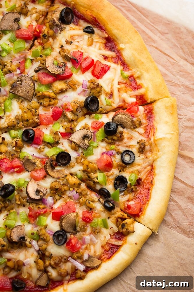 Close up of cooked vegan pizza with veggies, cheese, tempeh sausage, and tomato sauce