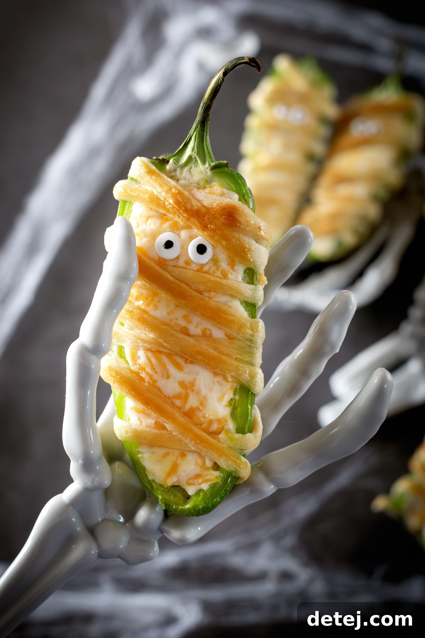 Serving plate of decorated mummy jalapeno poppers with candy eyes.