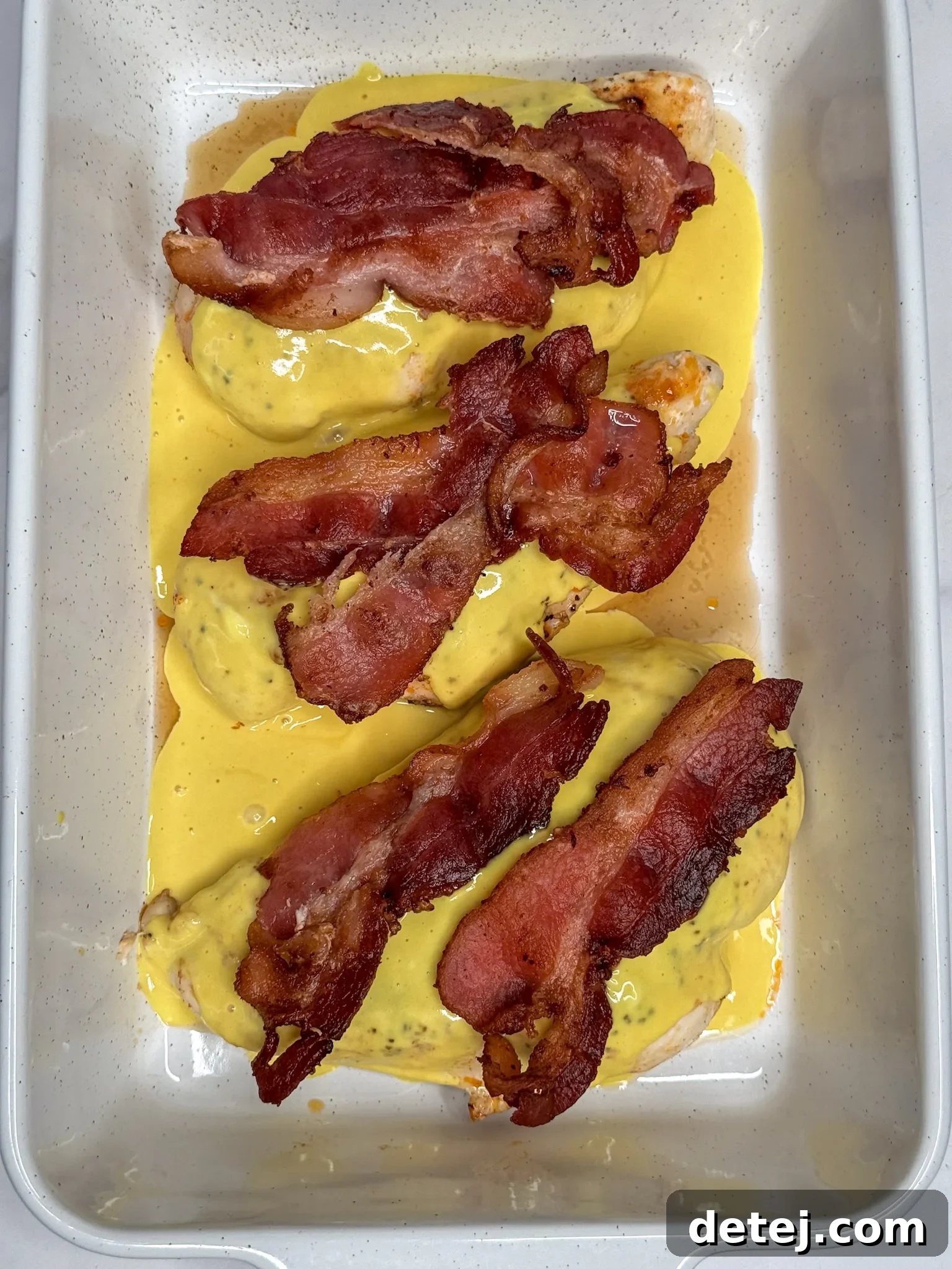 Alice Springs Chicken layered with honey mustard sauce, cheese, and bacon in a baking dish, before being placed in the oven.