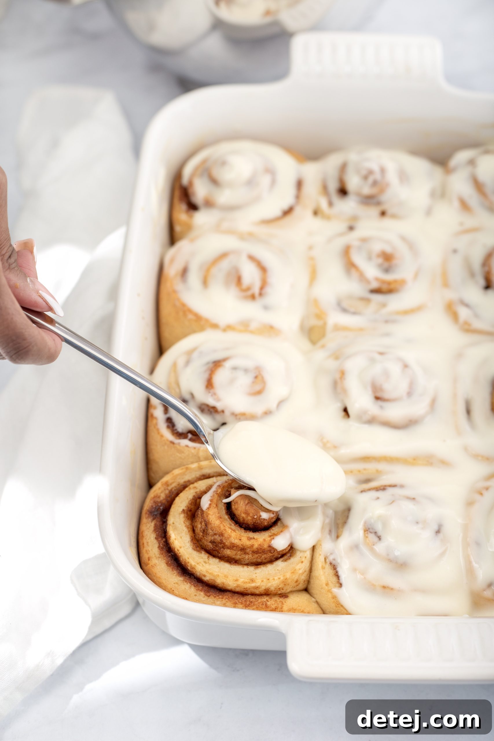 Close-up of fluffy cream cheese frosting being spread on warm cinnamon rolls