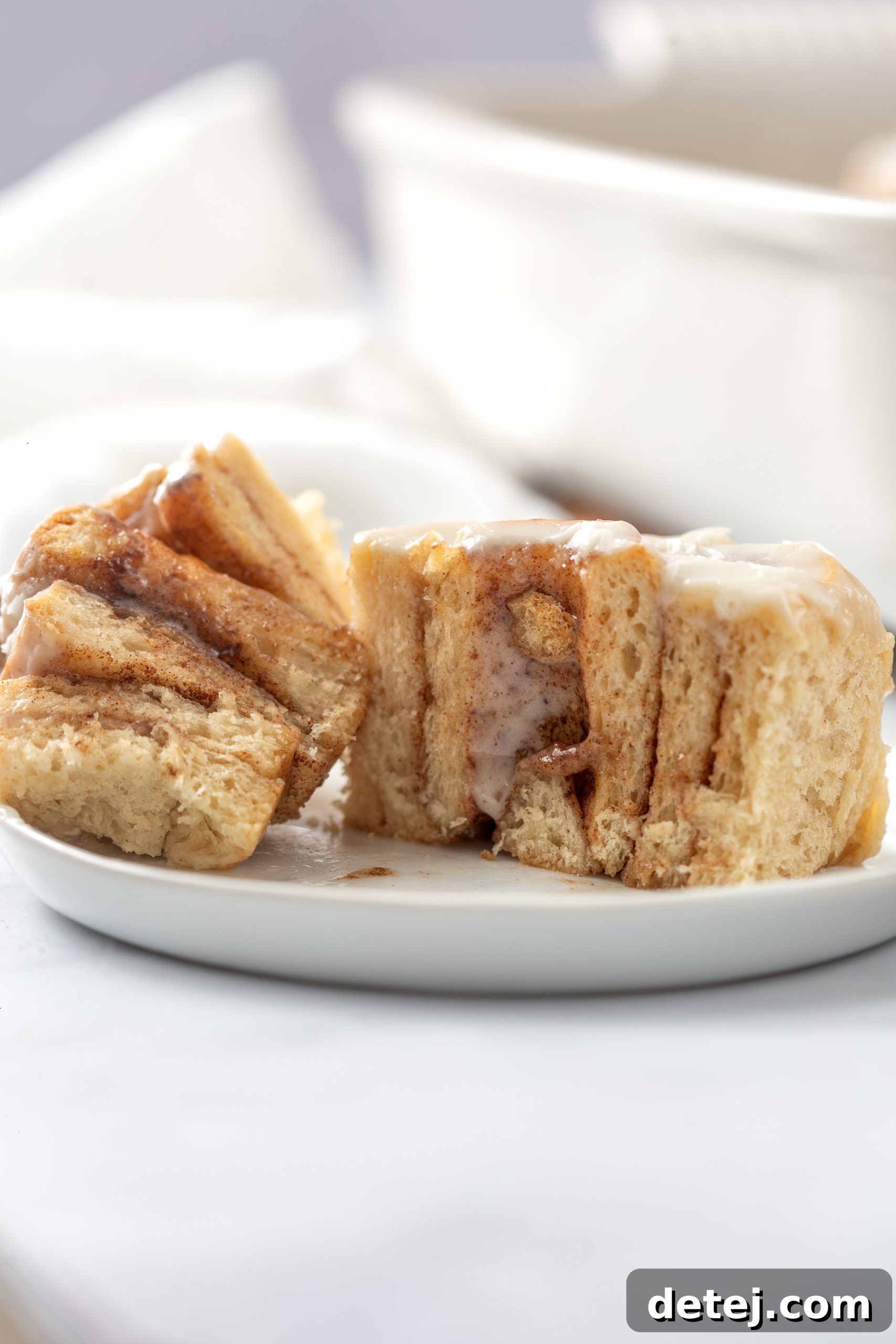 A hand reaching for a warm cinnamon roll from a baking dish