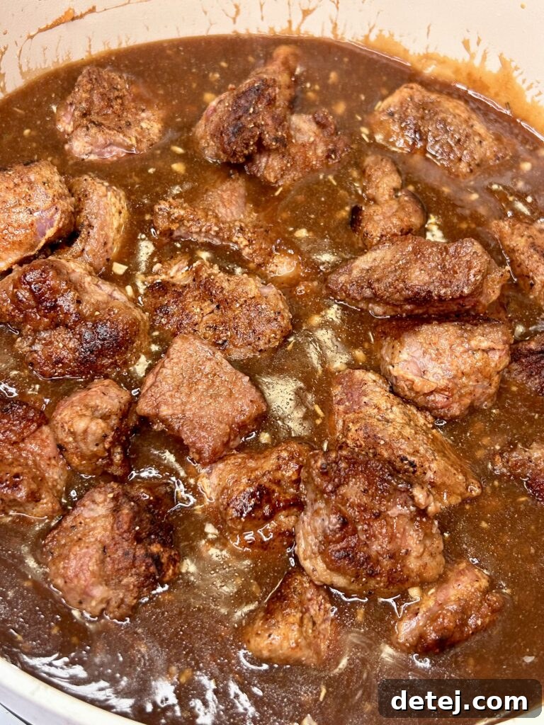 Close-up of beef tips simmering in thick, dark gravy.