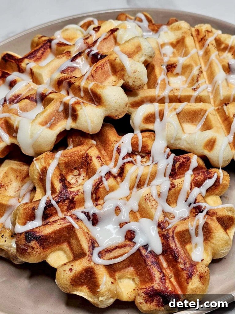 Finished Cinnamon Roll Waffles on a plate, ready to be served, topped with cream cheese icing.