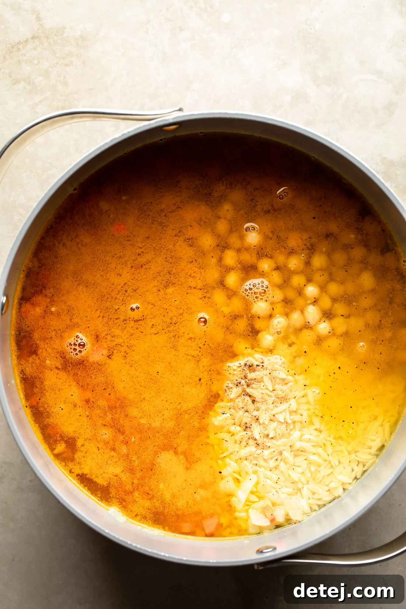 overhead view of the ingredients for Golden Orzo Soup with Chickpeas in a large pot.