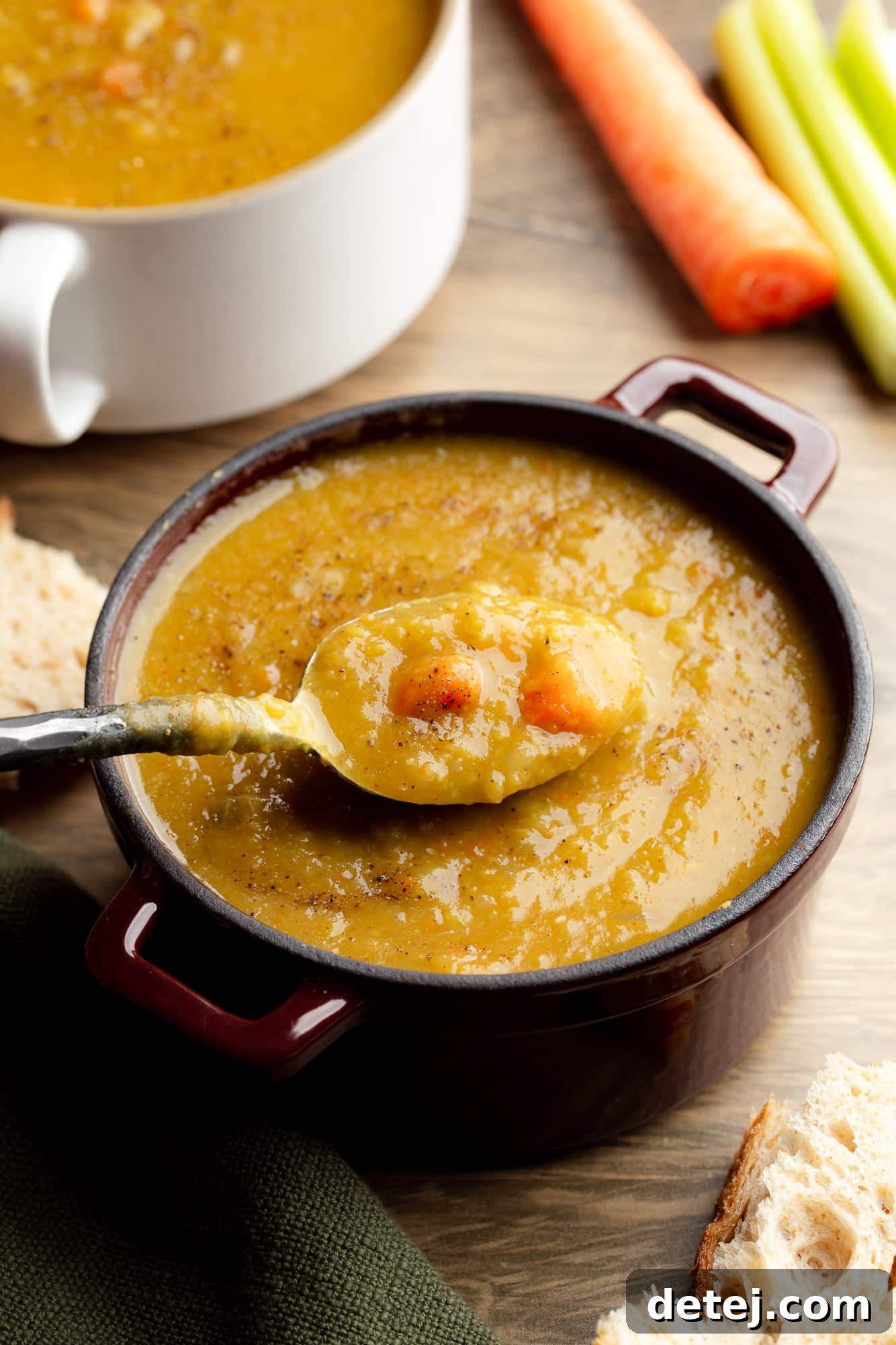 side view of a spoon being lifted out of a bowl of vegan split pea soup.