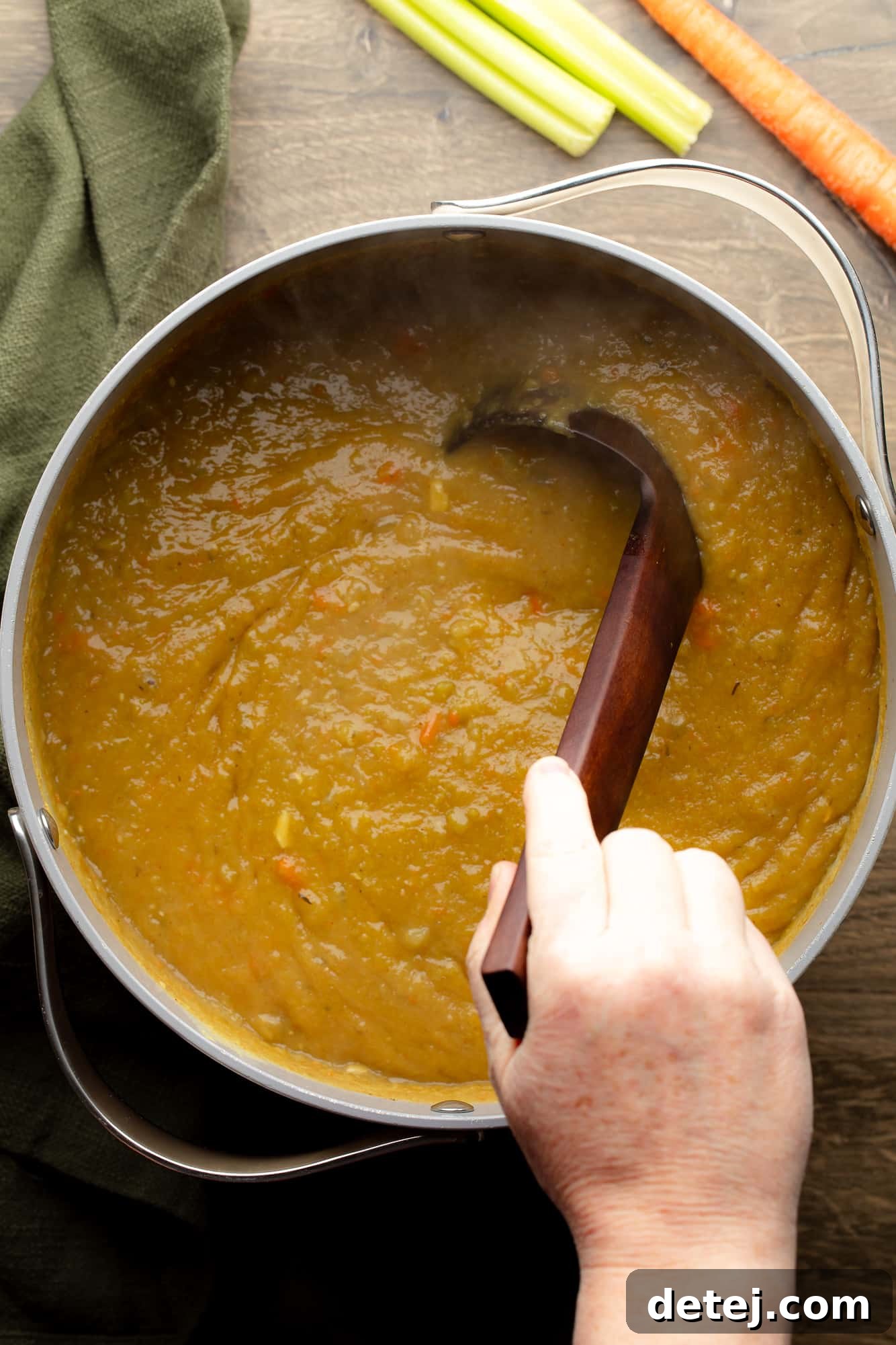 overhead view of a hand stirring a pot of vegan split pea soup with a ladle.