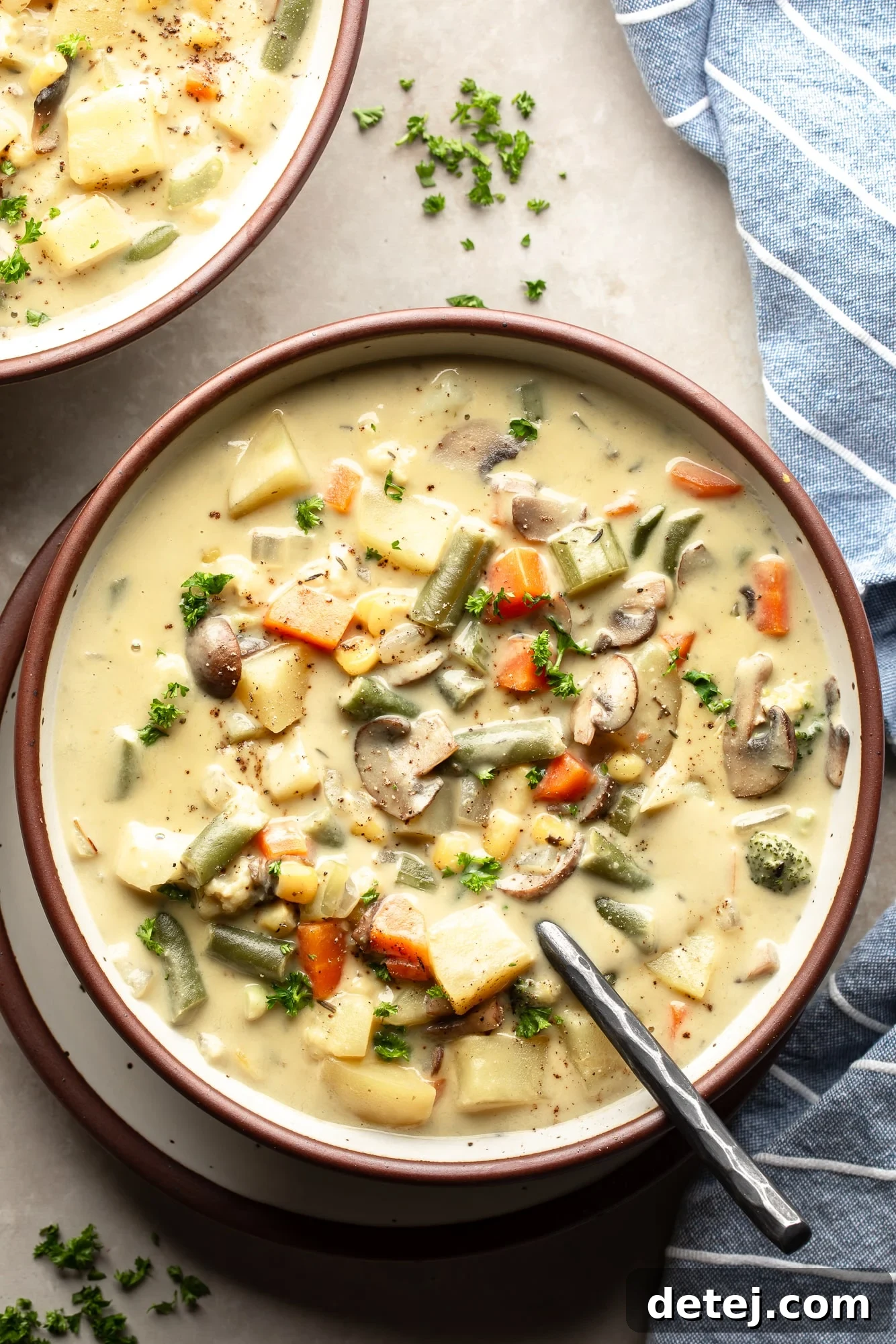 Close-up overhead view of a bowl of Creamy Vegetable Soup, garnished with fresh parsley and a side of rustic bread.