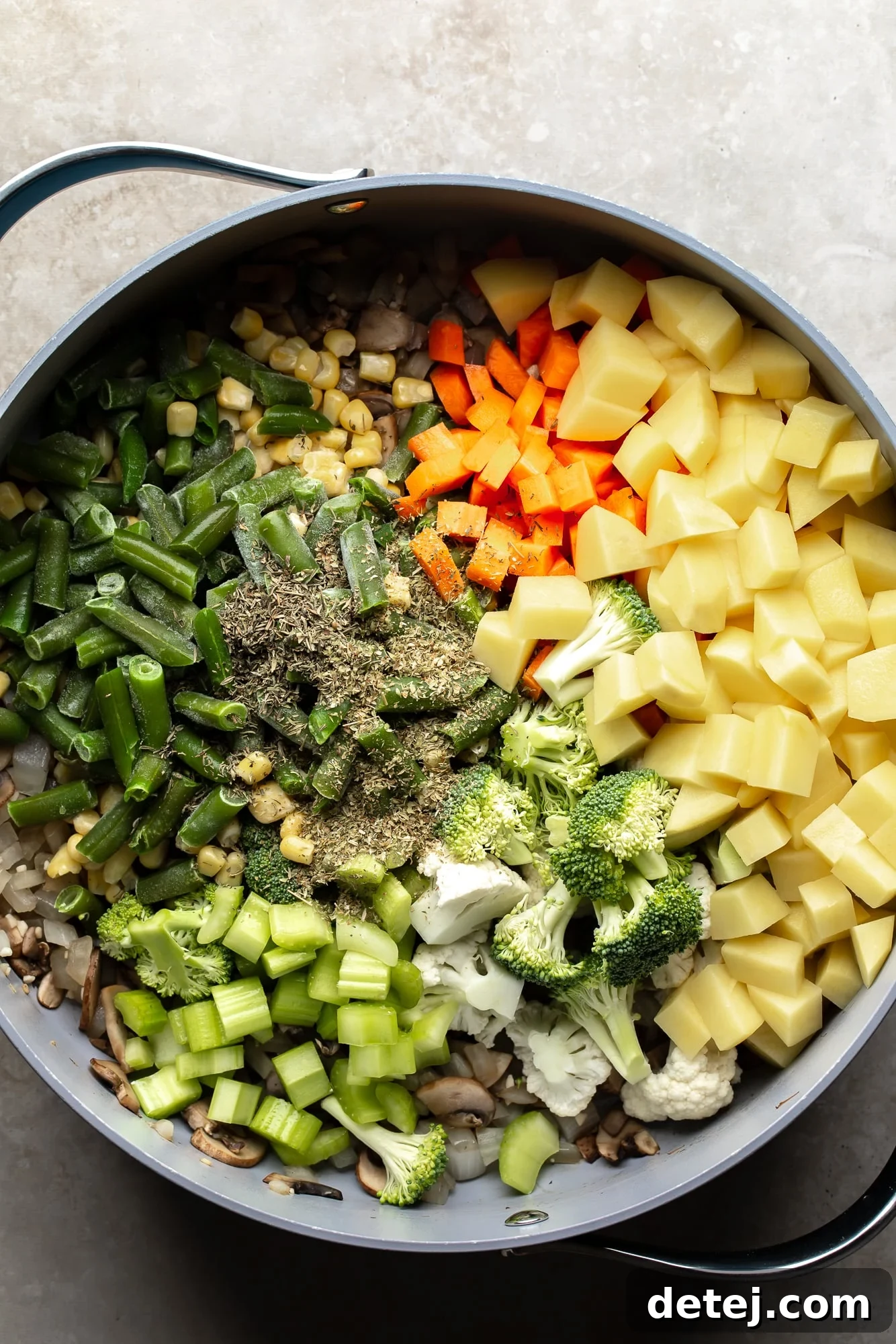 Overhead view of a medley of colorful vegetables and aromatic seasonings for Creamy Vegetable Soup in a large pot, ready for simmering and melding flavors.