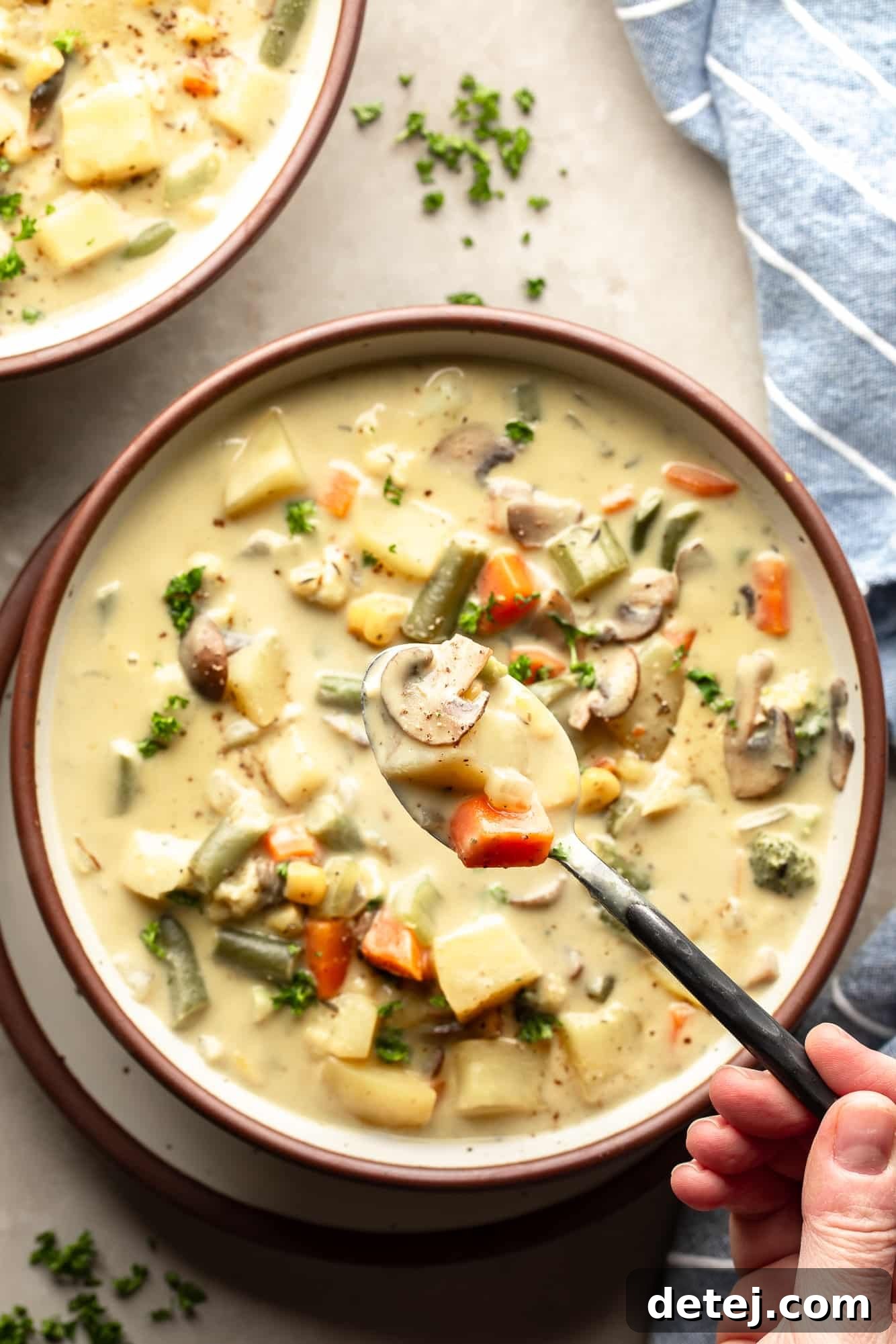 A hand holding a spoon filled with Creamy Vegetable Soup above a larger bowl of soup, showcasing its rich, inviting texture and vibrant colors.