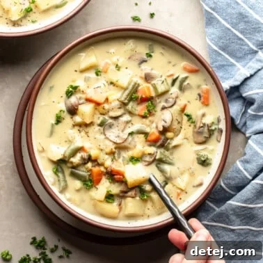 Overhead view of a person's hand holding a spoon in a bowl of Creamy Vegetable Soup, with a rustic background and fresh herbs.