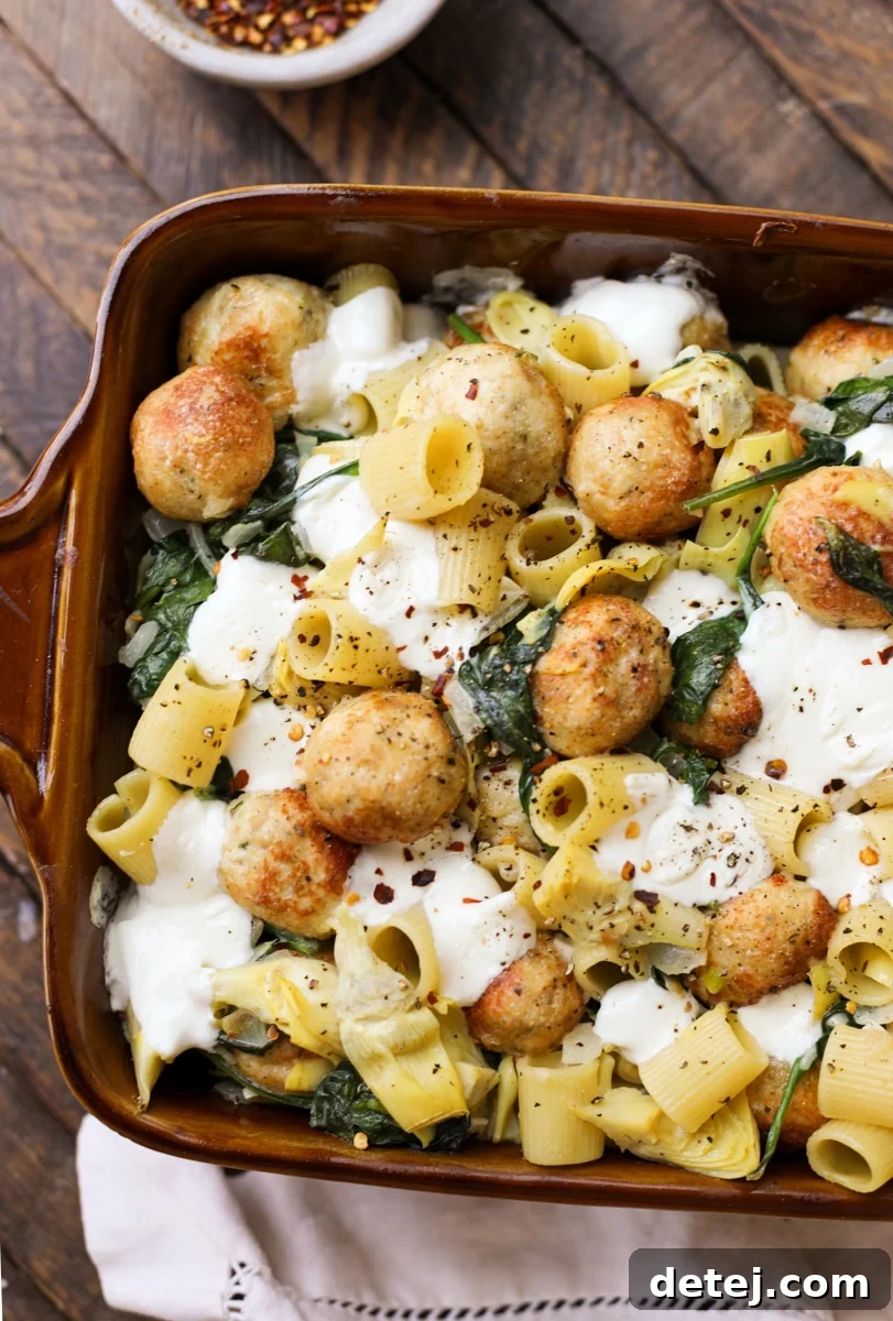 Delicious Creamy Spinach Artichoke Bake with Golden-Brown Chicken Meatballs and pasta in a ceramic dish, perfect comfort food