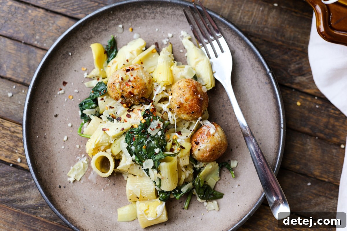 Serving of Creamy Spinach Artichoke Pasta Bake with Chicken Meatballs on a plate, garnished with fresh herbs