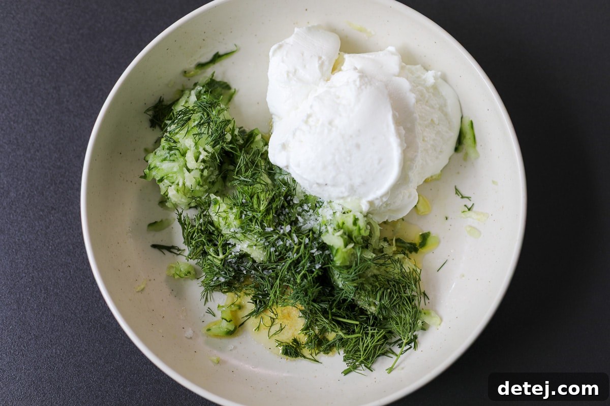 Close-up of fresh ingredients for easy tzatziki sauce in a bowl, including grated cucumber and fresh dill.