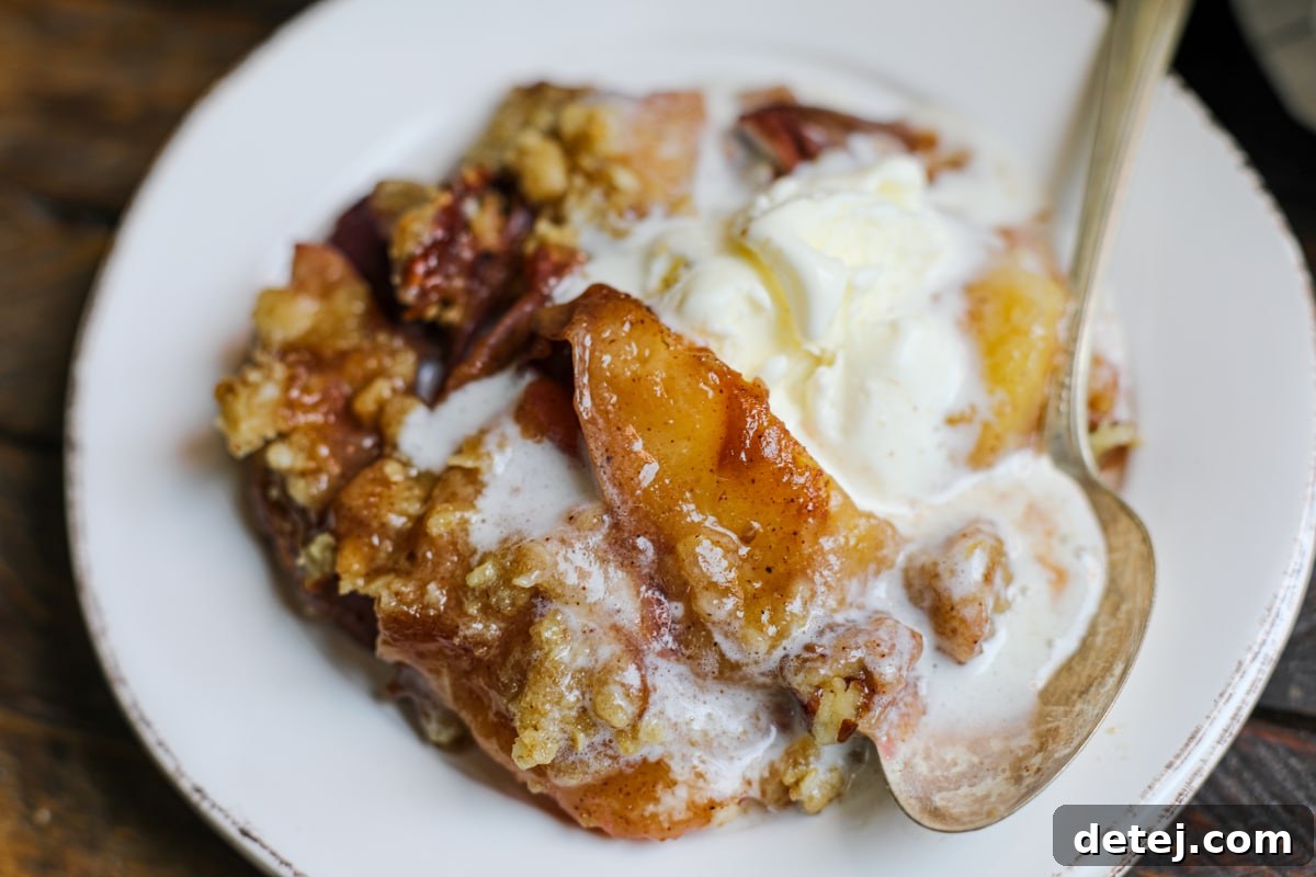 Scoop of peach crisp with melting vanilla ice cream in a white bowl