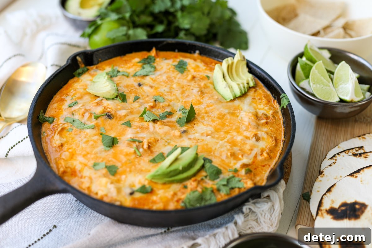 Close-up of bubbling Chicken Enchilada Dip in a cast iron pan, showing the rich texture and perfectly melted, golden-brown cheese before serving.