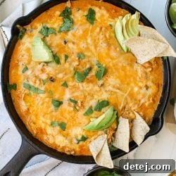 Close-up of Chicken Enchilada Dip in a cast iron skillet with a scoop taken out, showcasing the melted cheese and chicken.