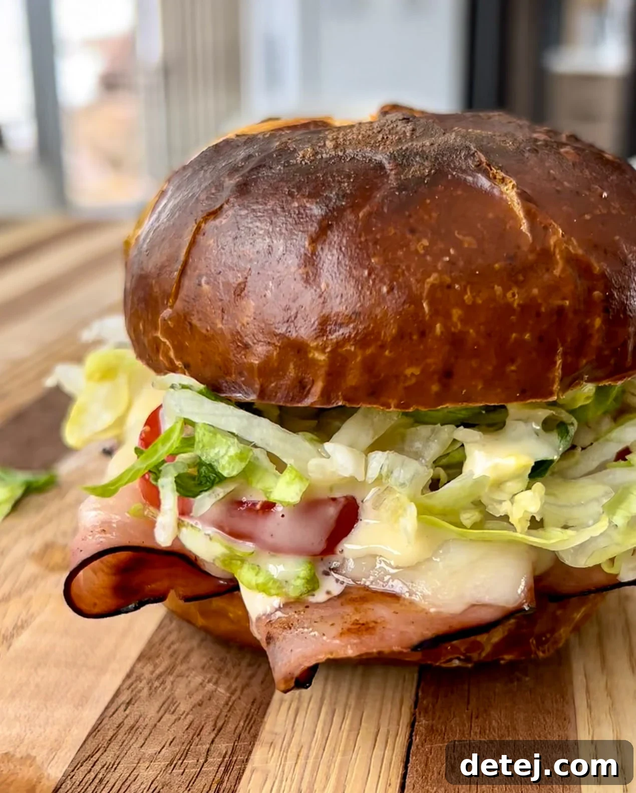 Decadent Black Forest Stack 3 Close-up of the delicious Black Forest Sandwich, showcasing the layers of ham, melted Swiss cheese, fresh lettuce, tomato, and honey mustard on a pretzel bun.