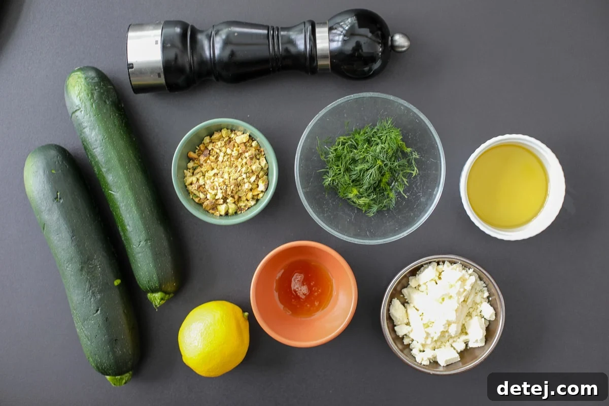 A collection of fresh ingredients laid out, including zucchini, a lemon, a bunch of dill, feta cheese, and pistachios, ready for cooking.
